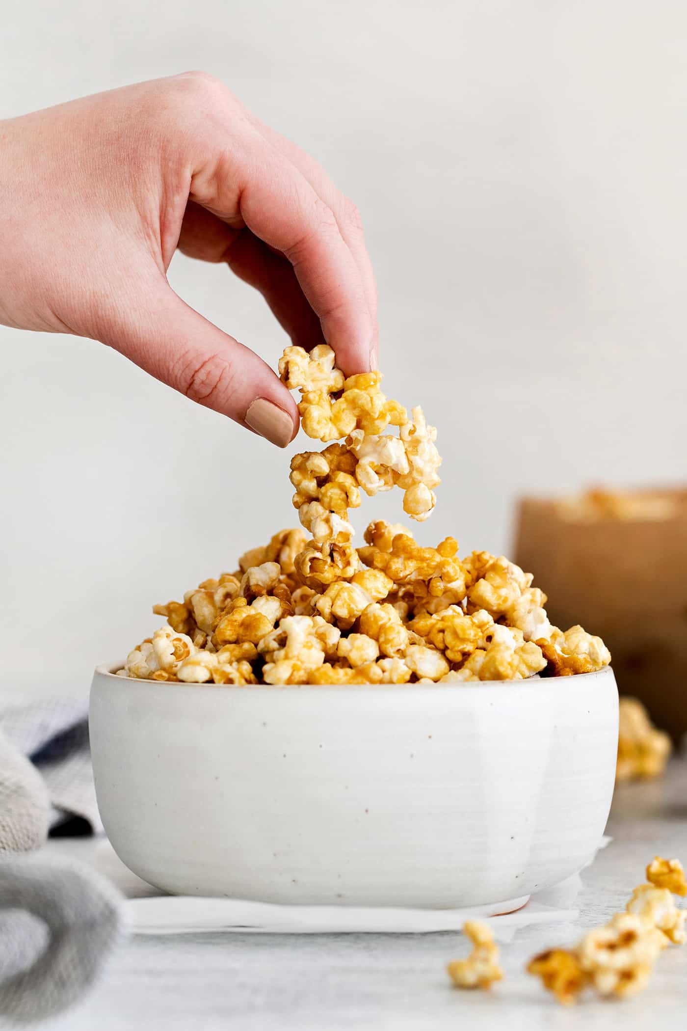 A hand grabbing a piece of caramel popcorn from a white bowl
