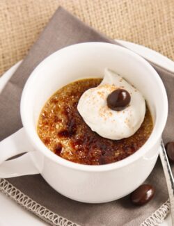 A white mug of creme brulee with whipped cream and a chocolate covered espresso bean