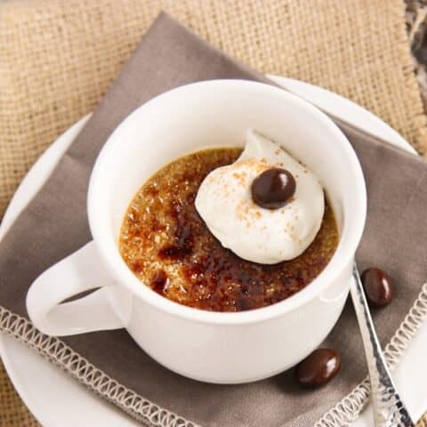 A white mug of creme brulee with whipped cream and a chocolate covered espresso bean