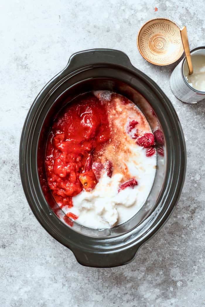 Overhead view of coconut milk, tomato paste, and crushed tomatoes added to crockpot