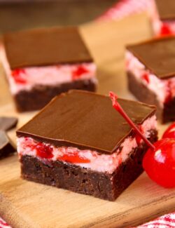Brownie squares with cherry frosting and chocolate glaze on a wooden board