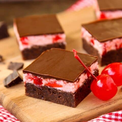 Brownie squares with cherry frosting and chocolate glaze on a wooden board