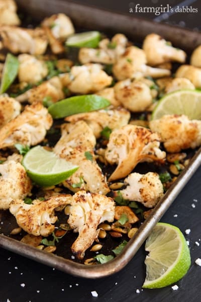 cauliflower, pepitas, and lime wedges on a rimmed pan