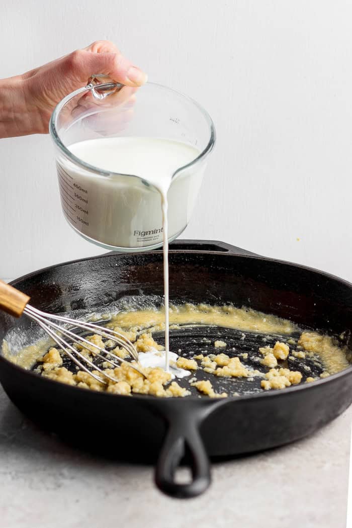This homemade stovetop macaroni and cheese recipe is perfect for a weeknight! Ultra creamy, rich, and much quicker than the baked version. Pouring milk into butter and flour for roux.