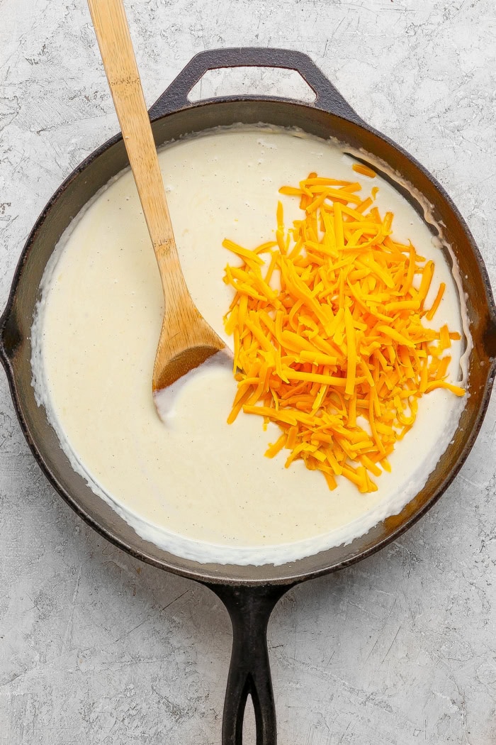 This homemade stovetop macaroni and cheese recipe is perfect for a weeknight! Ultra creamy, rich, and much quicker than the baked version. Stirring shredded cheddar into pan of cheese sauce.