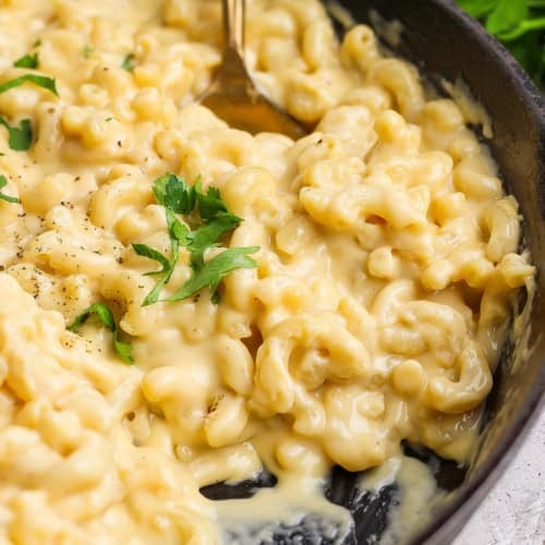 Spoon stirring macaroni and cheese in cast iron pan.