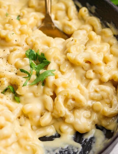 Spoon stirring macaroni and cheese in cast iron pan.