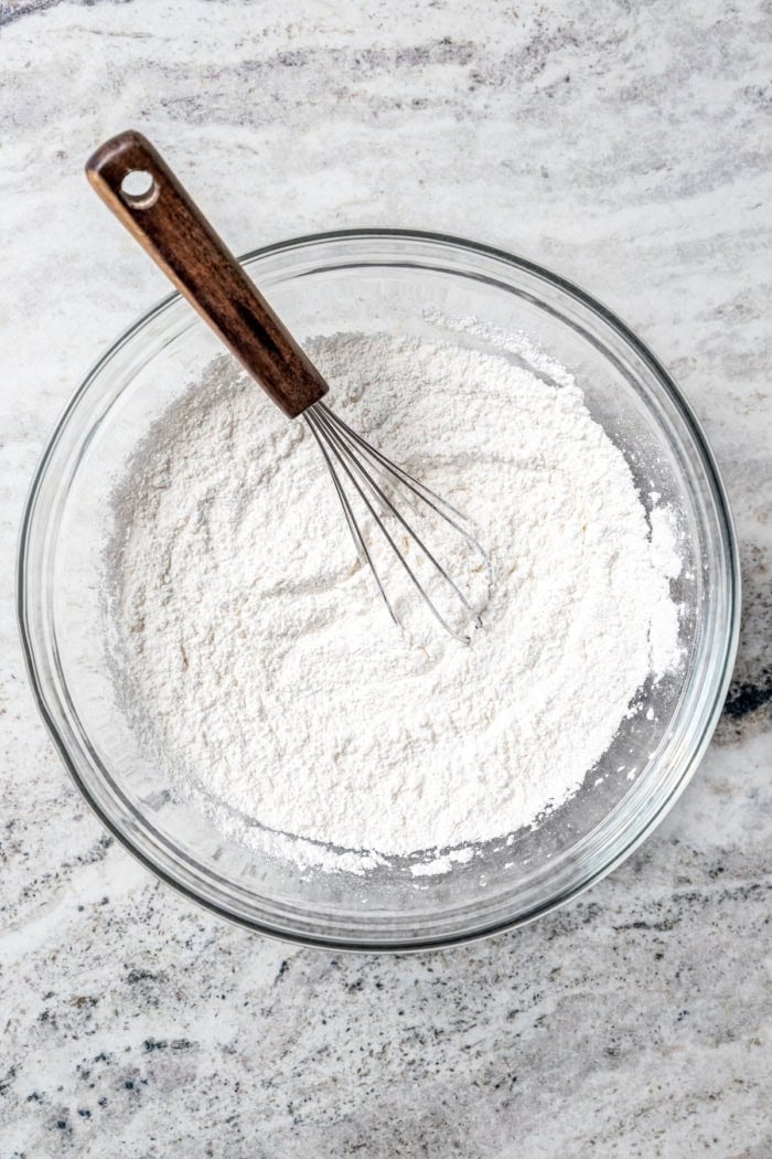 Overhead view of dry ingredients in glass mixing bowl with whisk