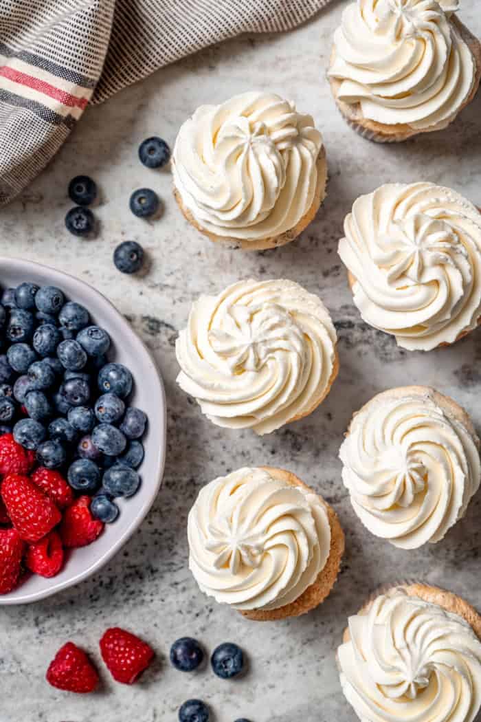 Overhead view of frosted angel food cupcakes with bowl of fresh berries