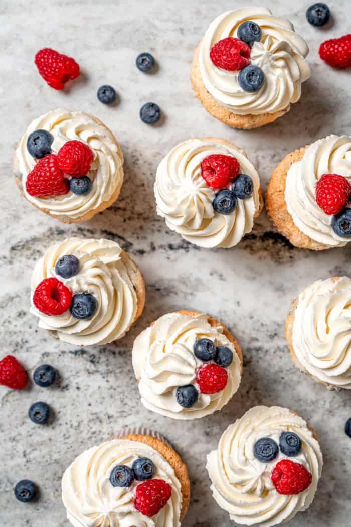 Overhead view of angel food cupcakes topped with frosting and fresh berries on marble countertop