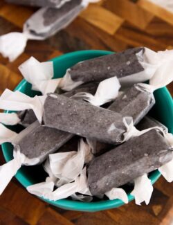 A bowl of black licorice pieces wrapped in wax paper