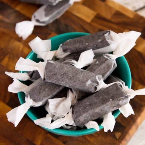 A bowl of black licorice pieces wrapped in wax paper