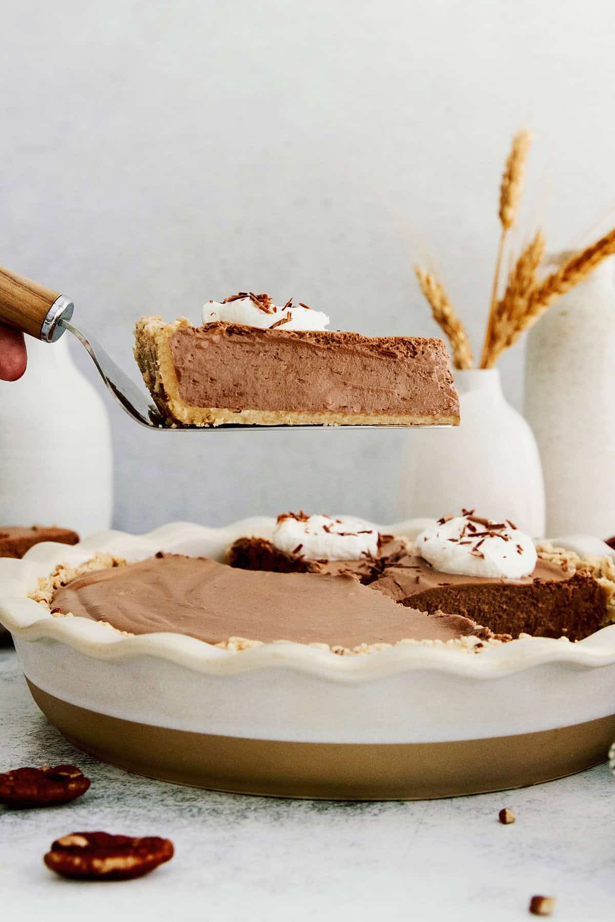 This lighter-than-air French silk pie recipe with 2 types of chocolate, espresso, and a salted pecan crust is a decadent holiday treat. Lifting a slice of decadent chocolatey pie with a cake spatula.