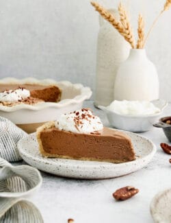 A slice of French silk pie on a serving plate with whipped sweetened cream and chocolate shavings on top.