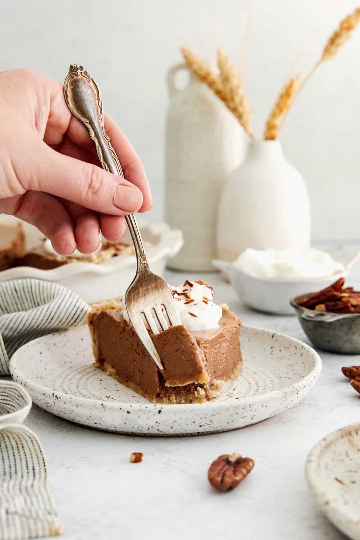This lighter-than-air French silk pie recipe with 2 types of chocolate, espresso, and a salted pecan crust is a decadent holiday treat. Digging into a slice of silky chocolate pie with whipped sweetened cream and chocolate shavings.
