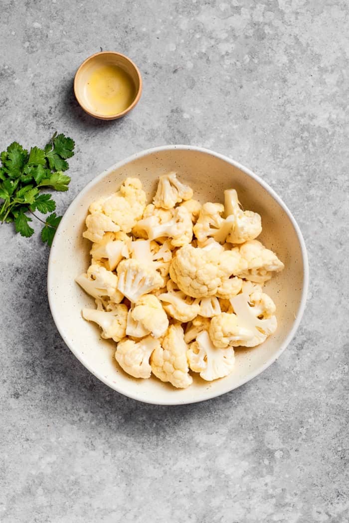 Bowl of raw cauliflower florets and bowl of oil.