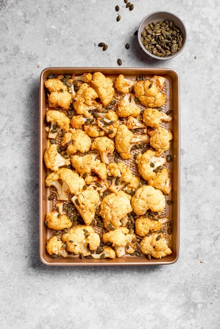 Pan of roasted cauliflower with pepitas set next to bowl of pepitas.
