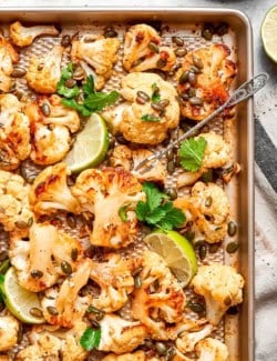 Mexican roasted cauliflower on sheet pan with pepitas, lime wedges, and cilantro.