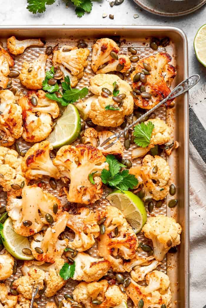Mexican roasted cauliflower on sheet pan with pepitas, lime wedges, and cilantro.