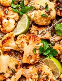 Mexican roasted cauliflower with pepitas, lime wedges, and cilantro.