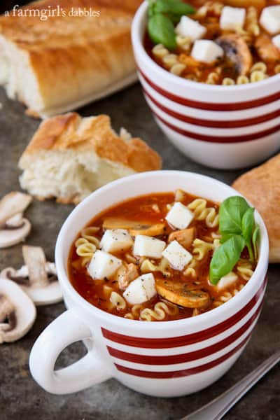 two mugs of Lasagna Soup with a loaf of bread and sliced mushrooms