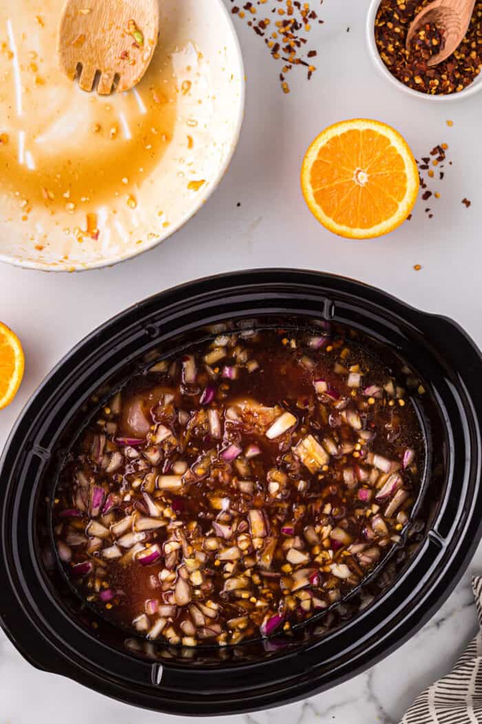 Chicken and orange sauce ingredients in a slow cooker