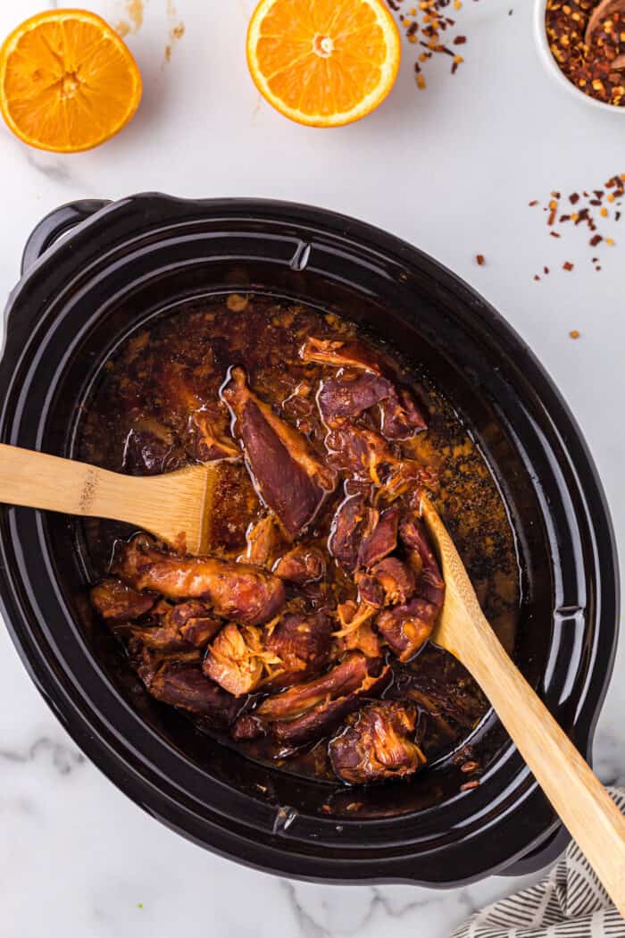 Two wooden spoons stirring chicken in a slow cooker