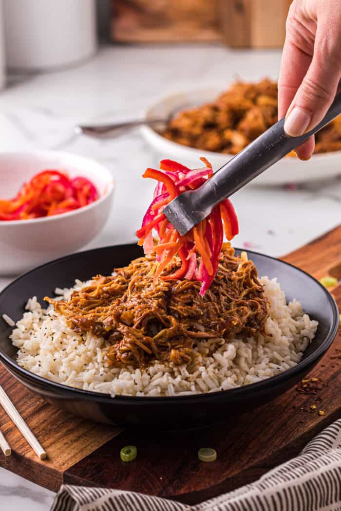 Orange chicken being topped with a fresh Asian slaw