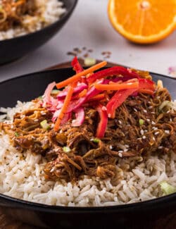 A black bowl of slow cooker orange chicken with fresh Asian slaw