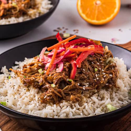 A black bowl of slow cooker orange chicken with fresh Asian slaw