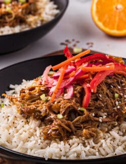 A black bowl of slow cooker orange chicken with fresh Asian slaw