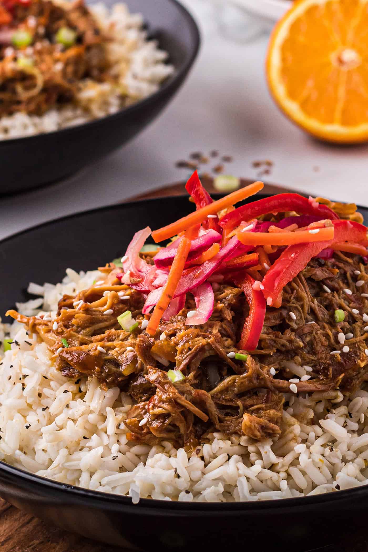 A black bowl of slow cooker orange chicken with fresh Asian slaw