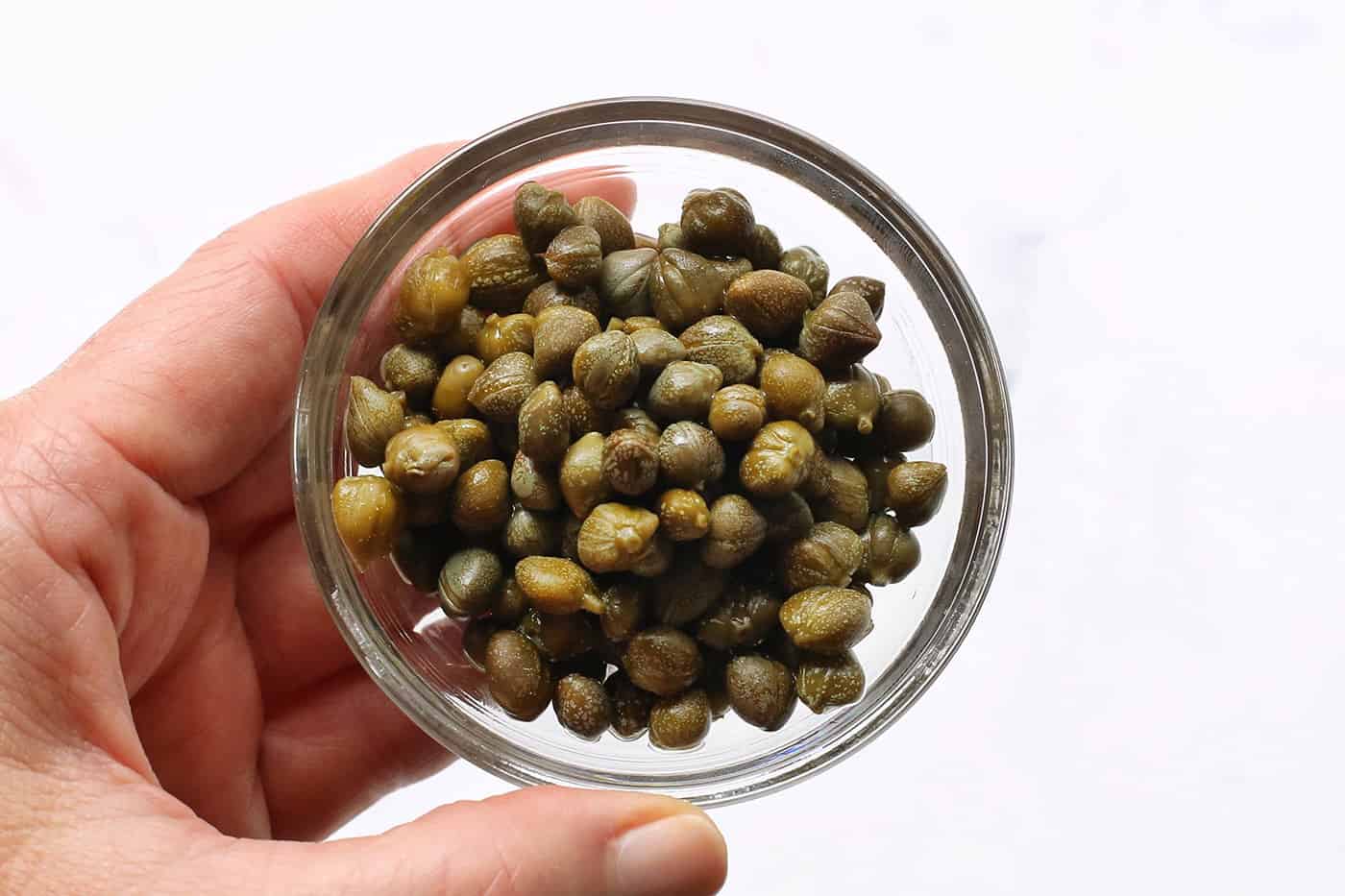 A hand holding a dish of capers