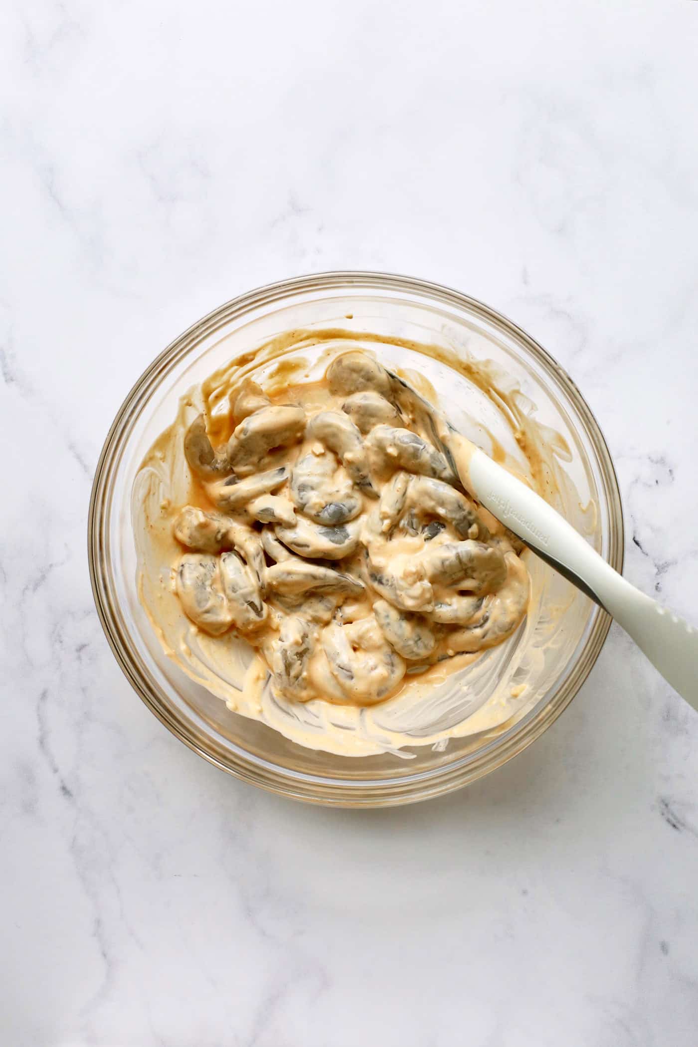 A spoon mixing sriracha mayo with shrimp.