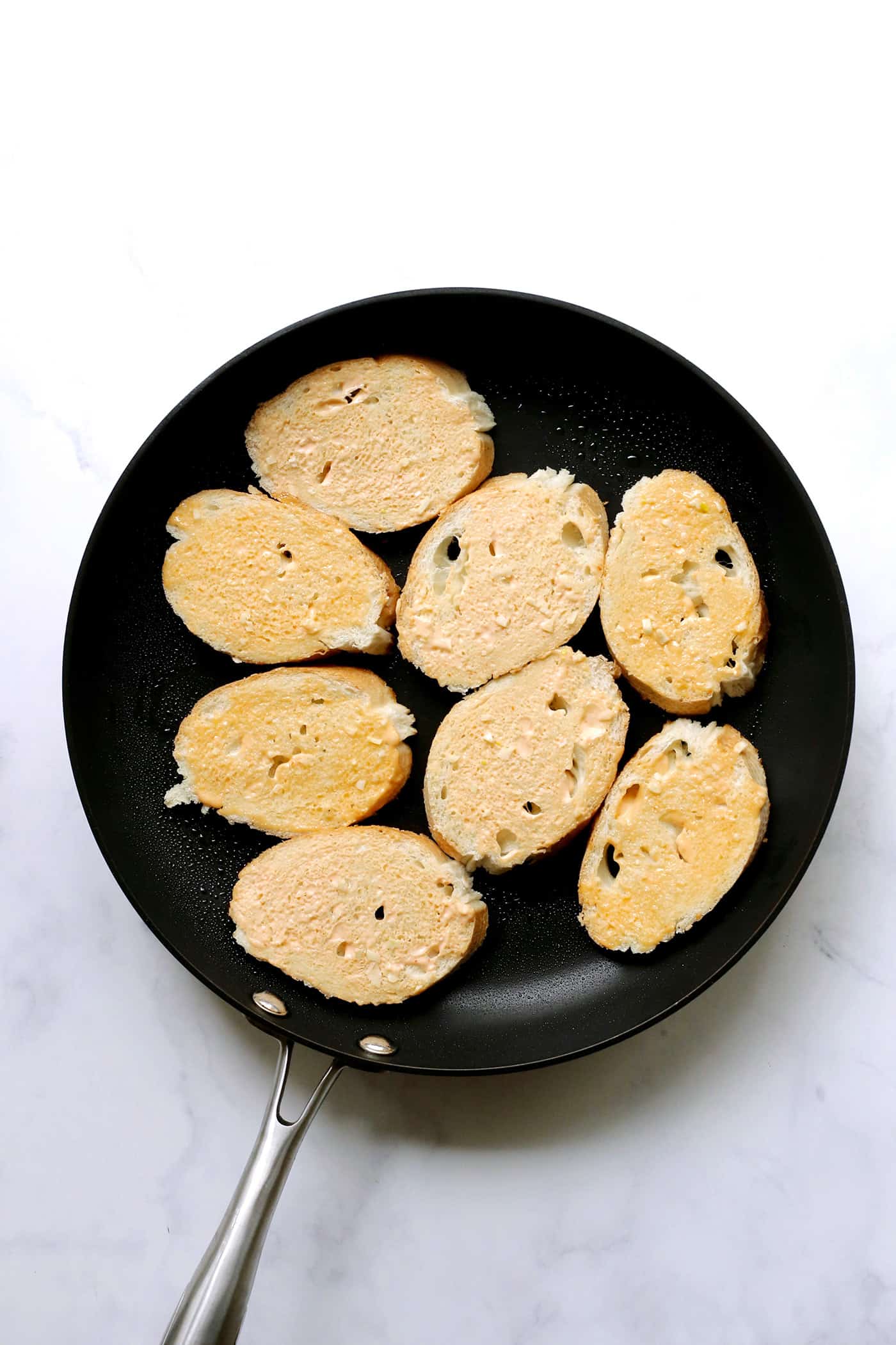 Slices of bread with sriracha mayo in a skillet.