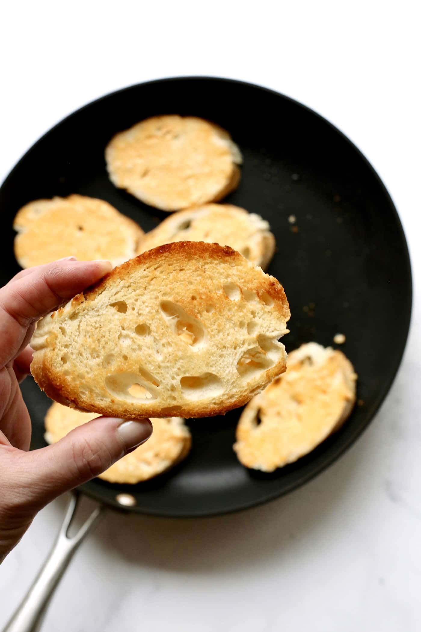 A hand holding a piece of toasted bread over a skillet