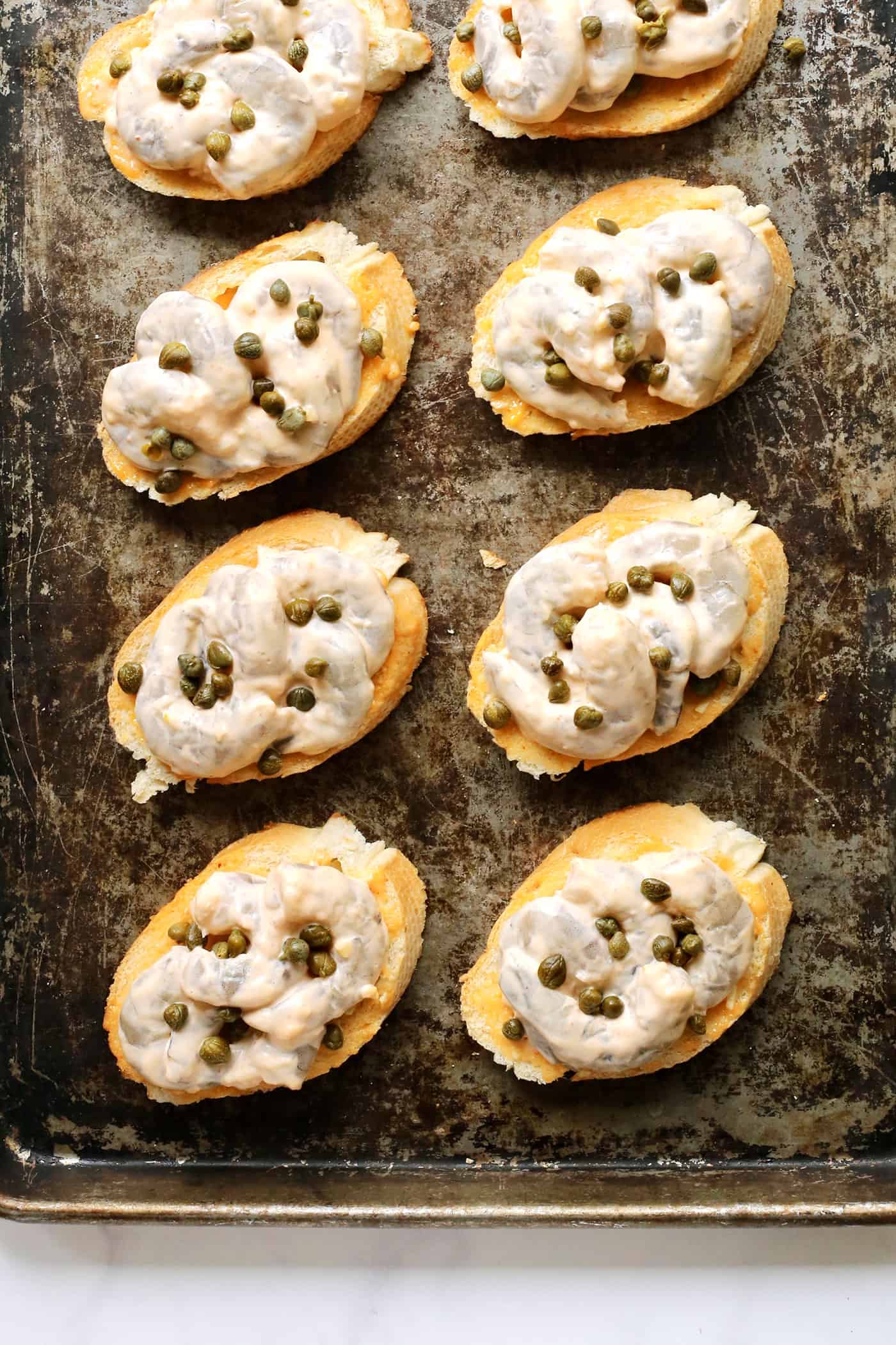 Shrimp toast topped with capers on a baking sheet.