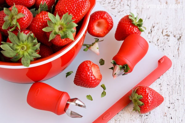 a bowl of strawberries and two OXO strawberry hullers