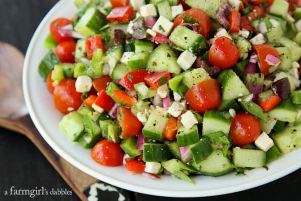 Greek Salad in a white serving bowl with a wood serving spoon