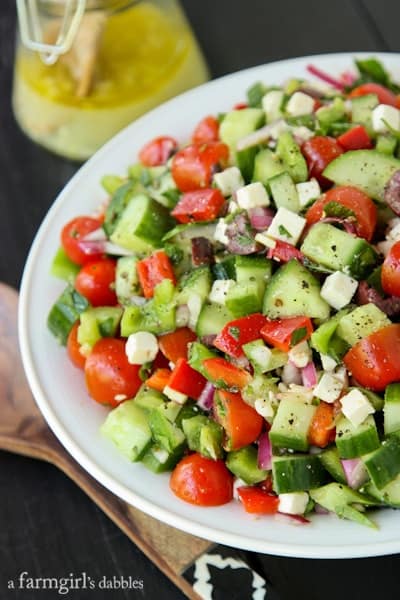 a white bowl of cucumbers, tomatoes, onions, and feta cheese