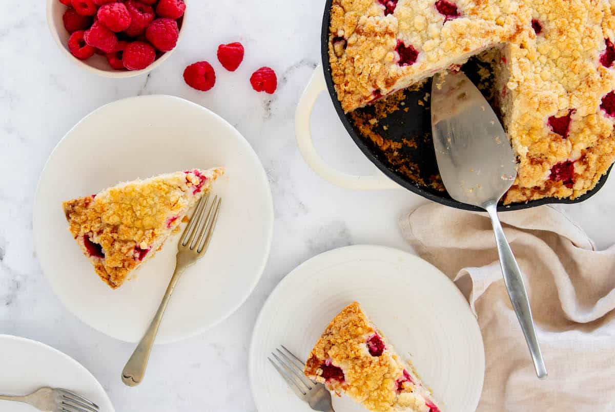 Two slices of rhubarb coffee cake on plates with the skillet of remaining cake in the background