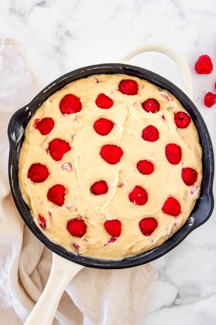 Coffee cake batter topped with raspberries in a cast iron skillet