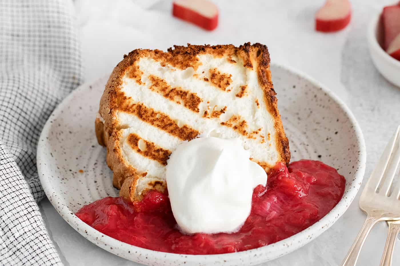 A slice of grilled angel food cake on a plate with raspberry sauce and whipped cream
