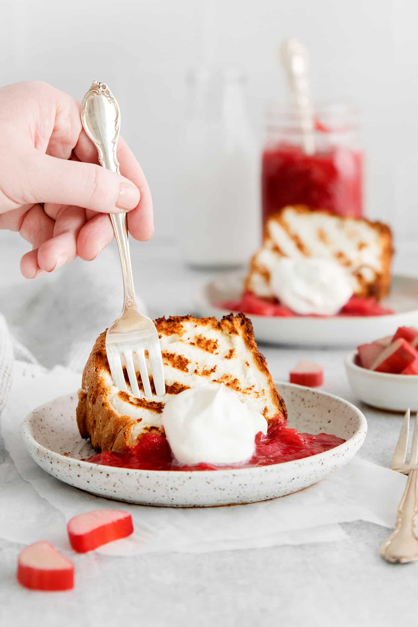 A fork diving into a slice of angel food cake with rhubarb sauce