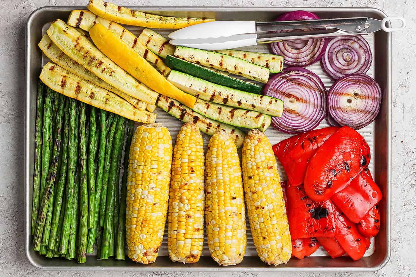 Overhead view of grilled vegetables on pan with tongs