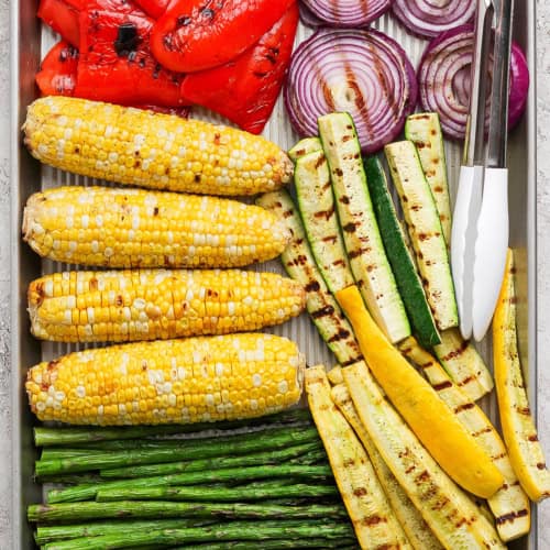 Closeup overhead view of grilled vegetables on pan with tongs