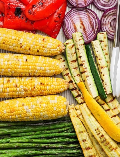 Closeup overhead view of grilled vegetables on pan with tongs