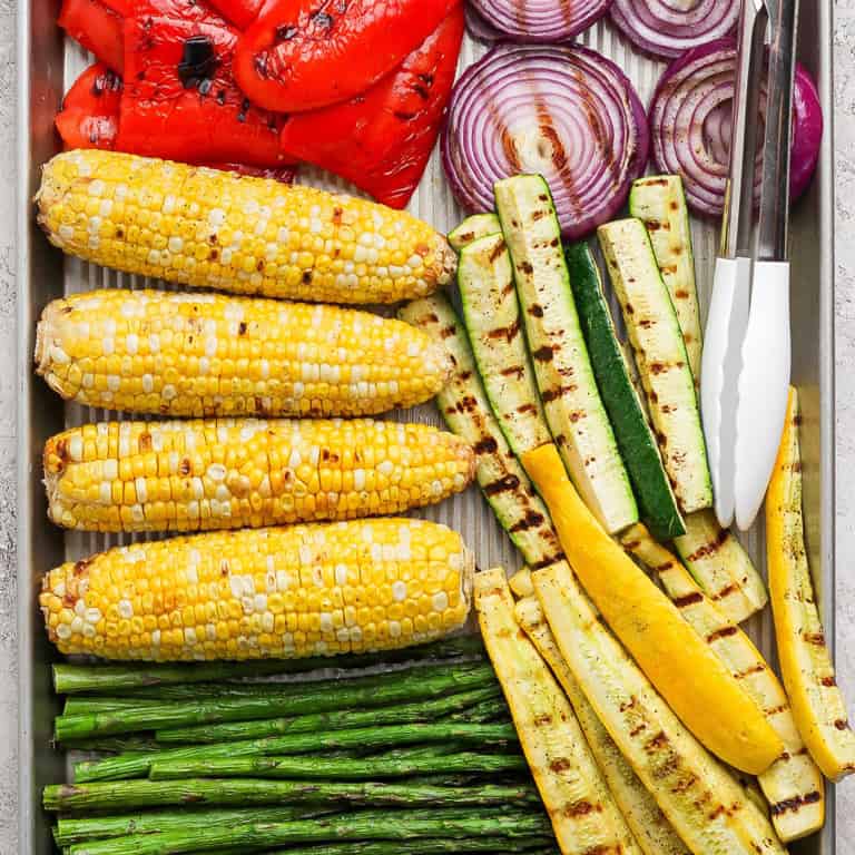 Closeup overhead view of grilled vegetables on pan with tongs