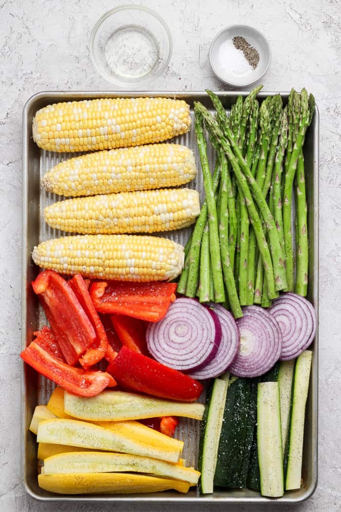 Overhead view of corn, asparagus, red bell pepper, onion, and summer squash on sheet pan