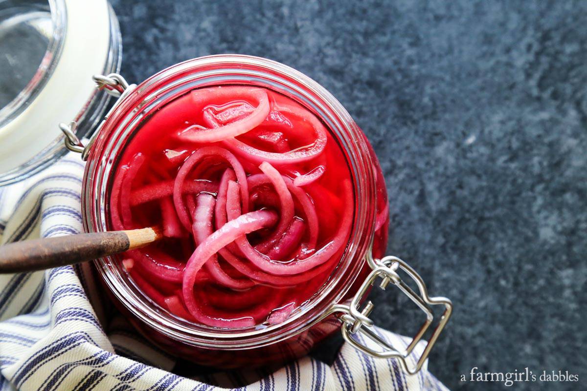 pickled onions in a jar with a wood serving spoon